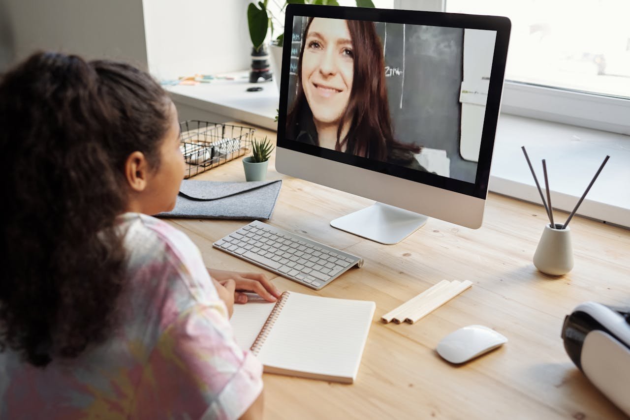 A teenage girl participates in a virtual class, focused on the screen in a home setting.